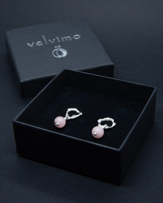 Hopeiset eripari nappikorvakorut orgaanisella muotoilulla ja vaaleanpunaisilla kivihelmillä kuvattuna mustassa pahvisessa Valvimo-korurasissa.
